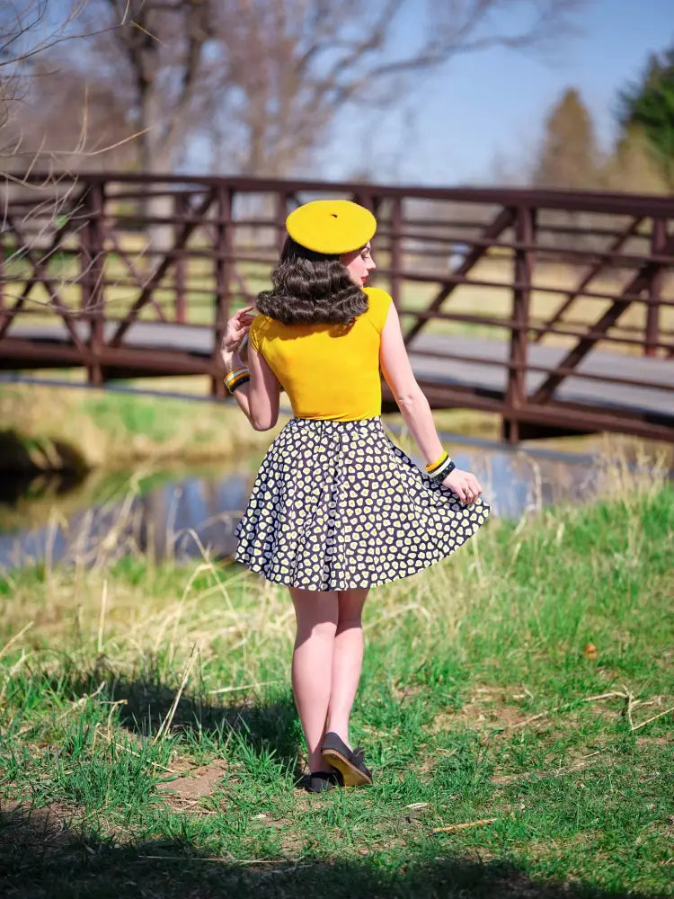 A woman wearing a yellow sleeveless top with a black and white sunny side up polka dot skater skirt and matching yellow beret