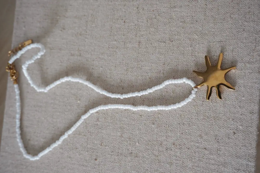 A delicate white seed bead necklace with a gold-toned sun-shaped pendant from Sunseeker collection