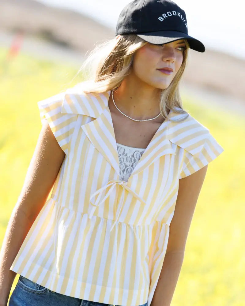 Yellow and white vertically striped cotton sleeveless blouse with ruffled collar peplum hem and front tie detail