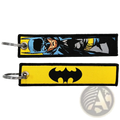 Two superhero embroidered keychains featuring a blue and yellow comic-style batman design and a black bat symbol on yellow fabric