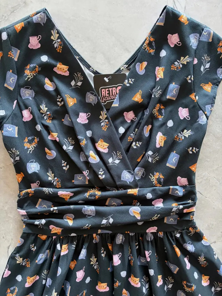 Black satin Greta Tea Party wrap dress with pockets featuring pastel pink orange and blue teapot and floral pattern