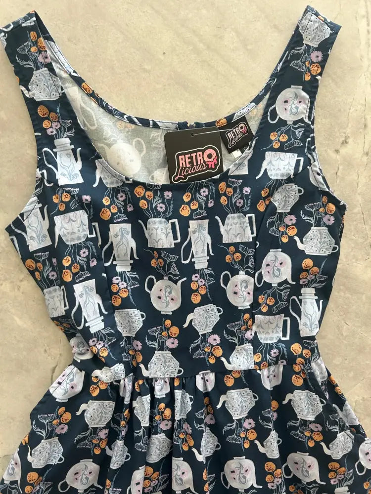 A navy blue cotton sleeveless fit and flare midi dress with white teapots and orange flowers and a ruffled hemline