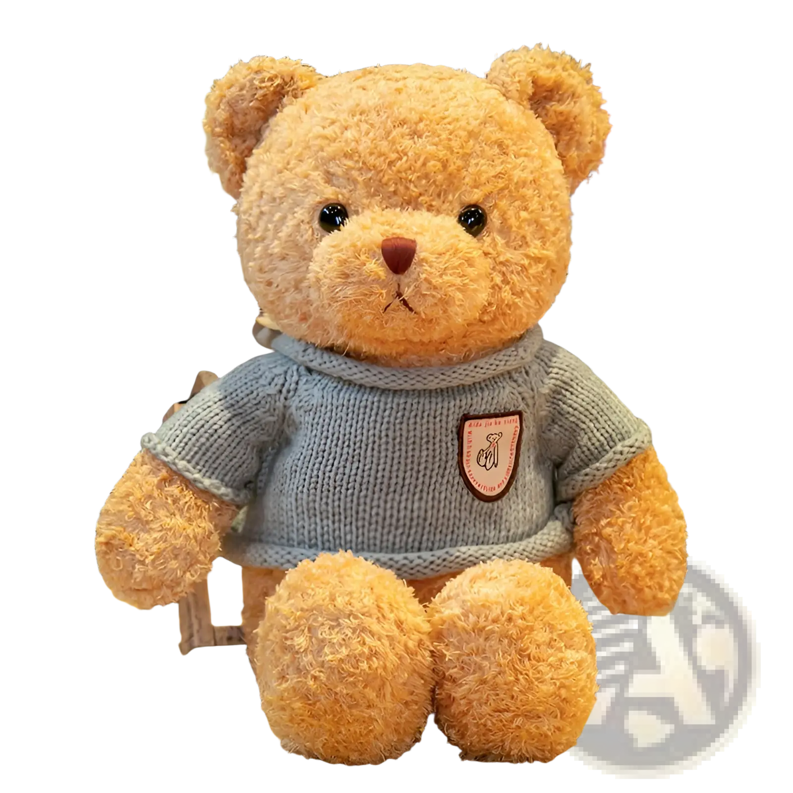 A plush tan teddy bear plush toy wearing a light blue knitted sweater with a pink and brown patch on chest
