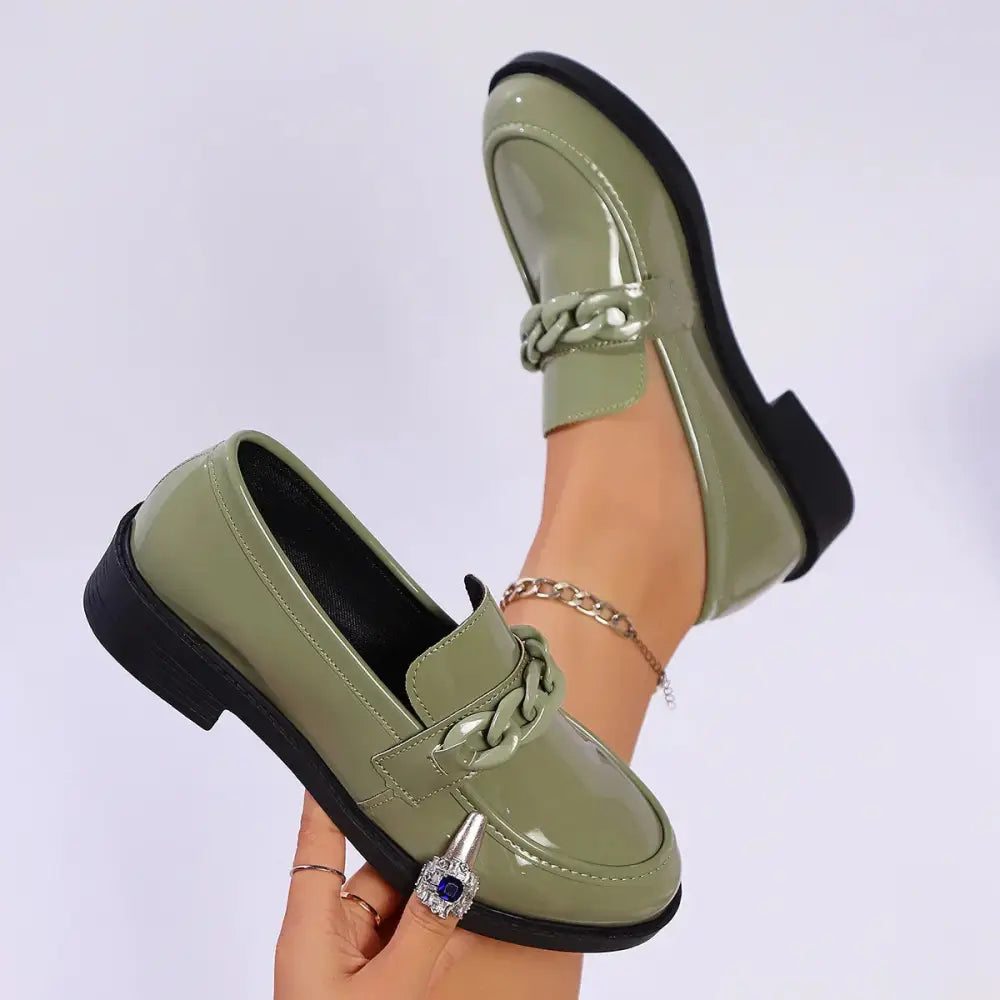Olive green patent leather chunky chain loafers with a chain-link strap and blue gemstone accent on the toe