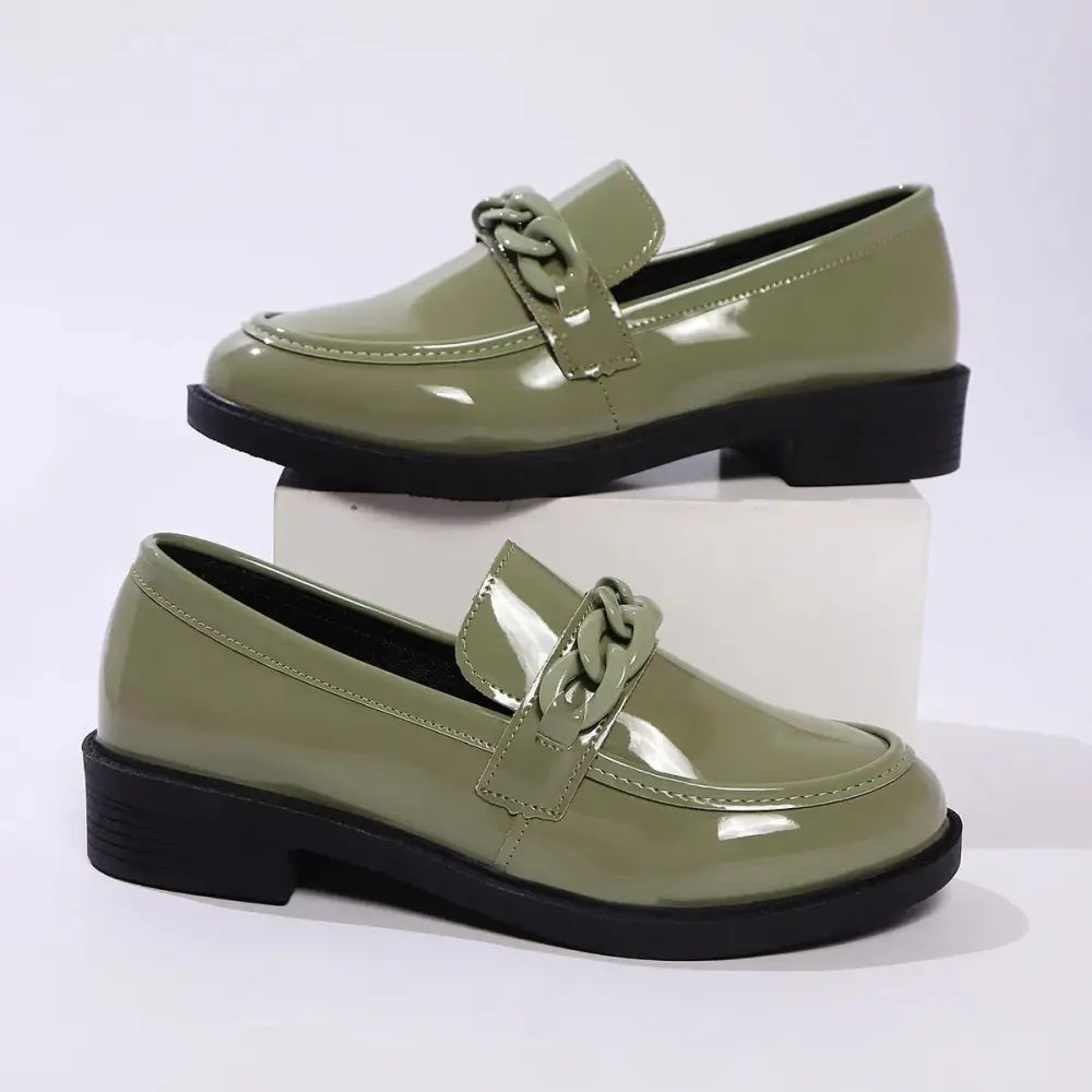 Olive green patent leather loafers with a chunky black sole and decorative chain-link strap across the toe