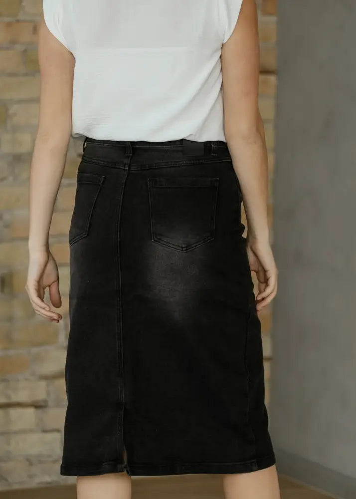 Black denim midi skirt with a high waisted straight cut and back pockets shown from the back side