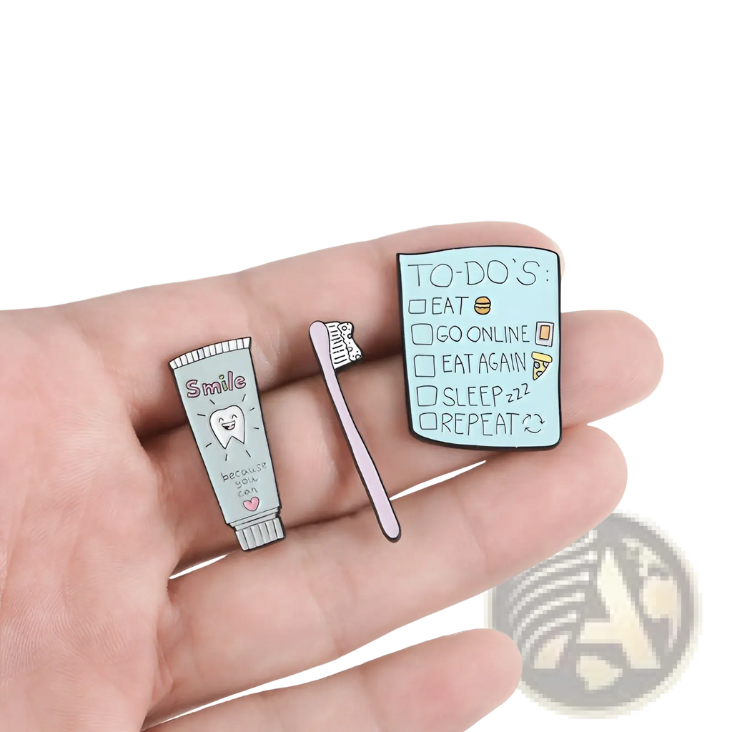 Three enamel pins featuring a cartoon toothpaste smile, pink toothbrush, and light blue checklist for dental care