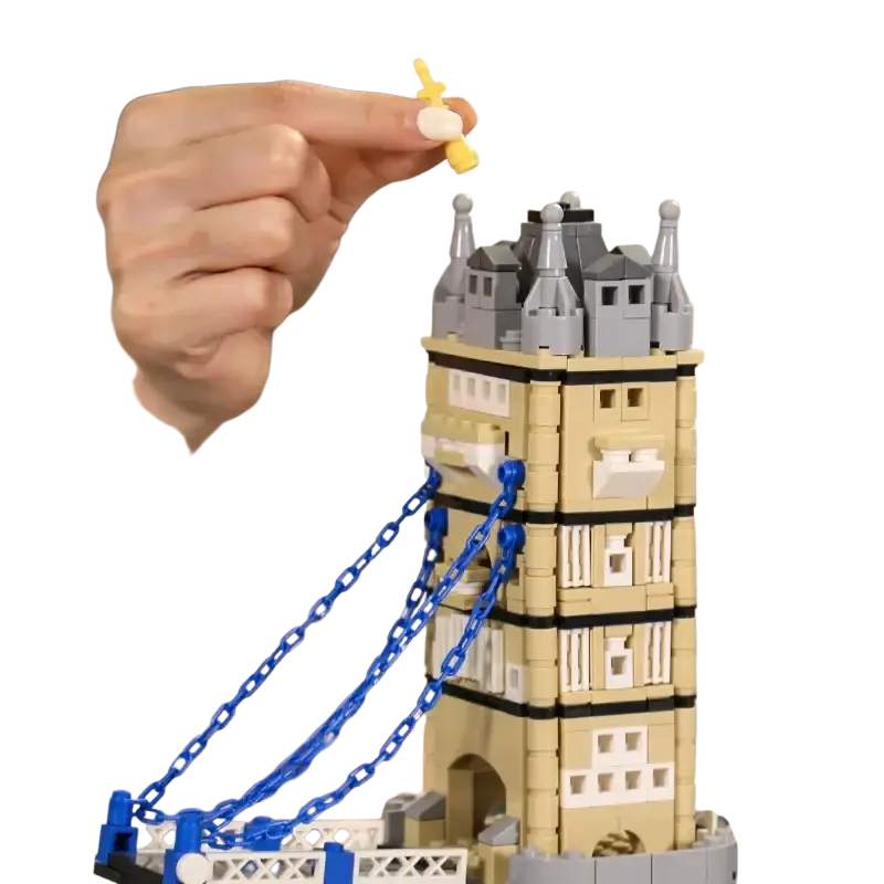 A beige and gray lego tower bridge building brick architecture model with blue chains being assembled by a hand