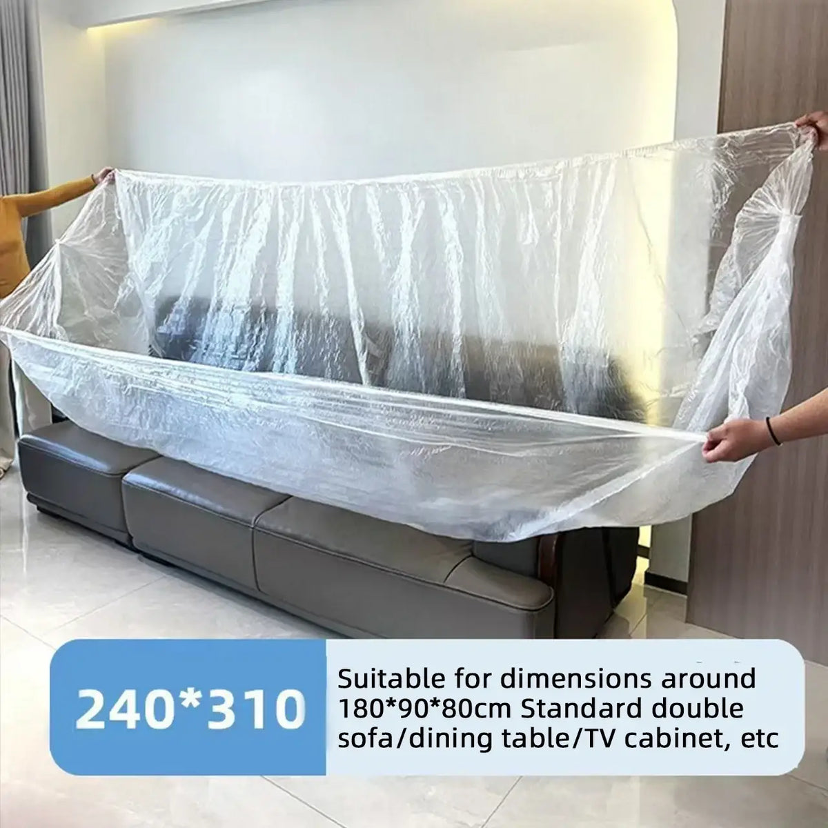 Clear plastic furniture dust cover being stretched over a dark gray leather sofa for protection against dust