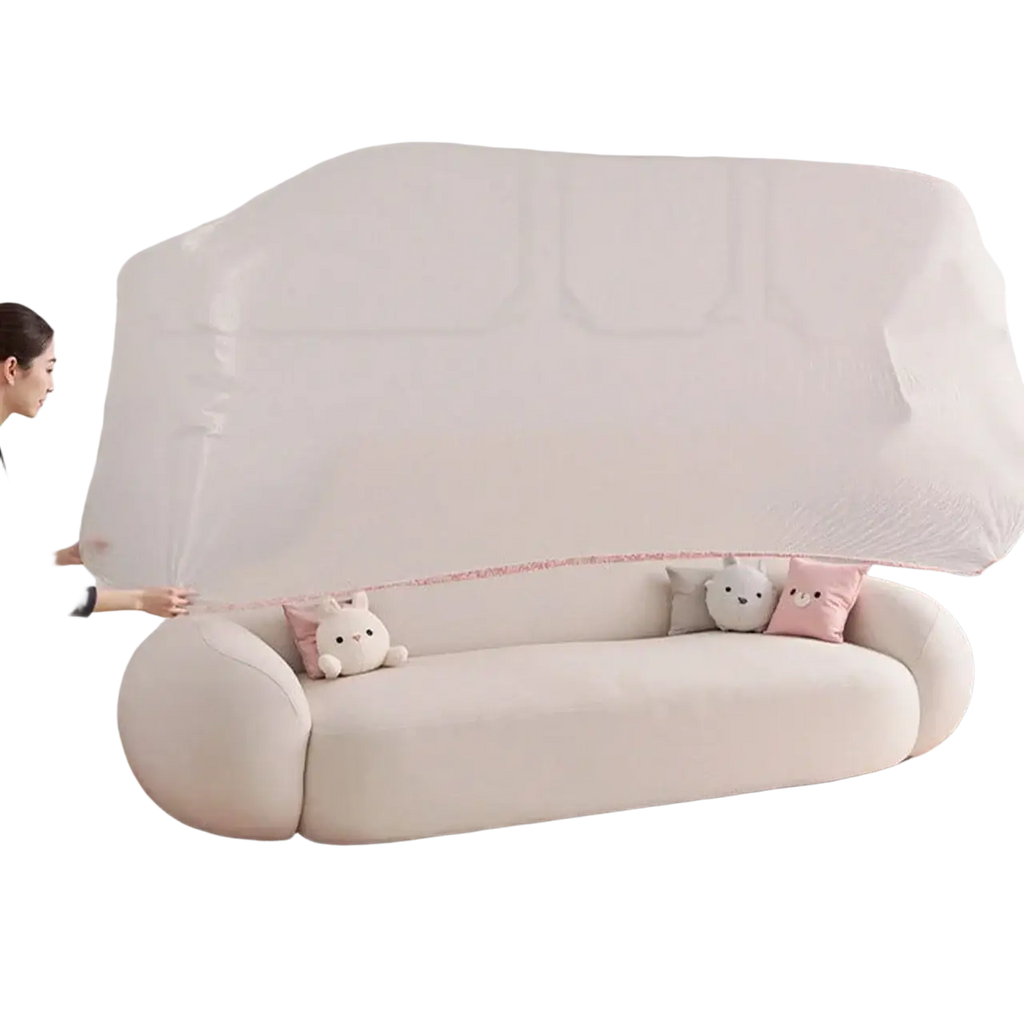 Cream-colored plush sofa with rounded arms and stuffed animal pillows covered by transparent plastic furniture dust cover