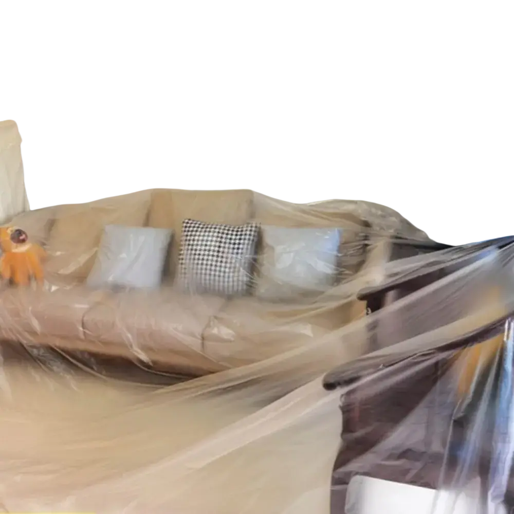 Beige sofa covered in a transparent plastic furniture dust cover protector with light blue and black-and-white pillows visible