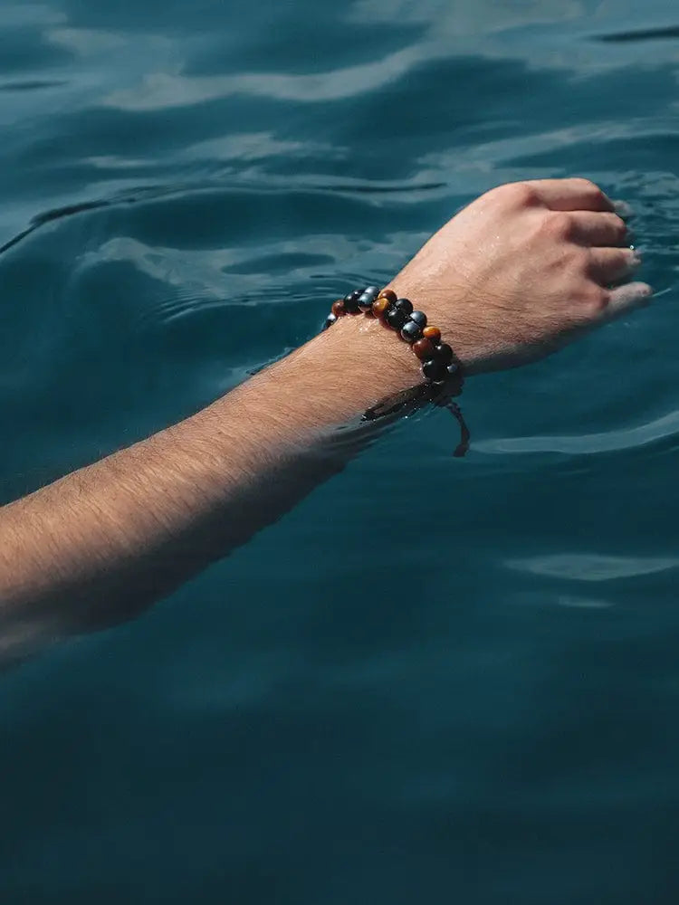 A triple protection tiger eye beaded bracelet with alternating brown and black stones worn on a wrist with adjustable cord