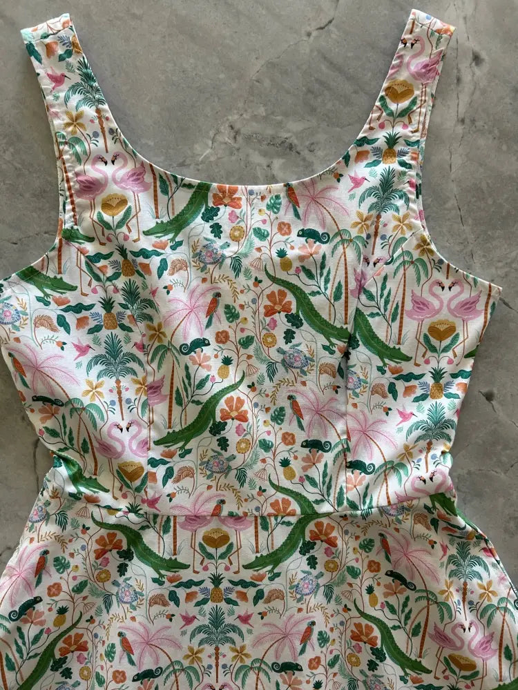 A vibrant tropical flamingo and alligator print sleeveless skater dress on white fabric with lush green foliage