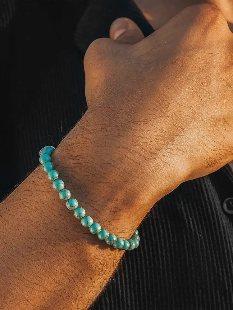 A turquoise stone beaded bracelet with smooth marbled stones and a silver clasp worn on a wrist