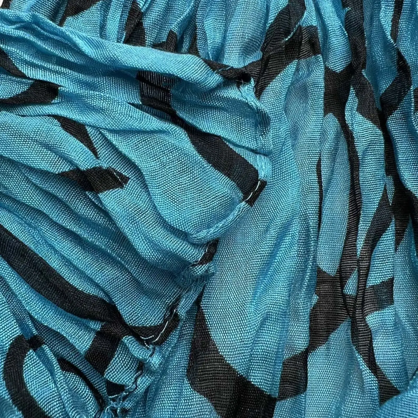 A soft flowing turquoise crinkle beach cover up scarf with bold black abstract patterns