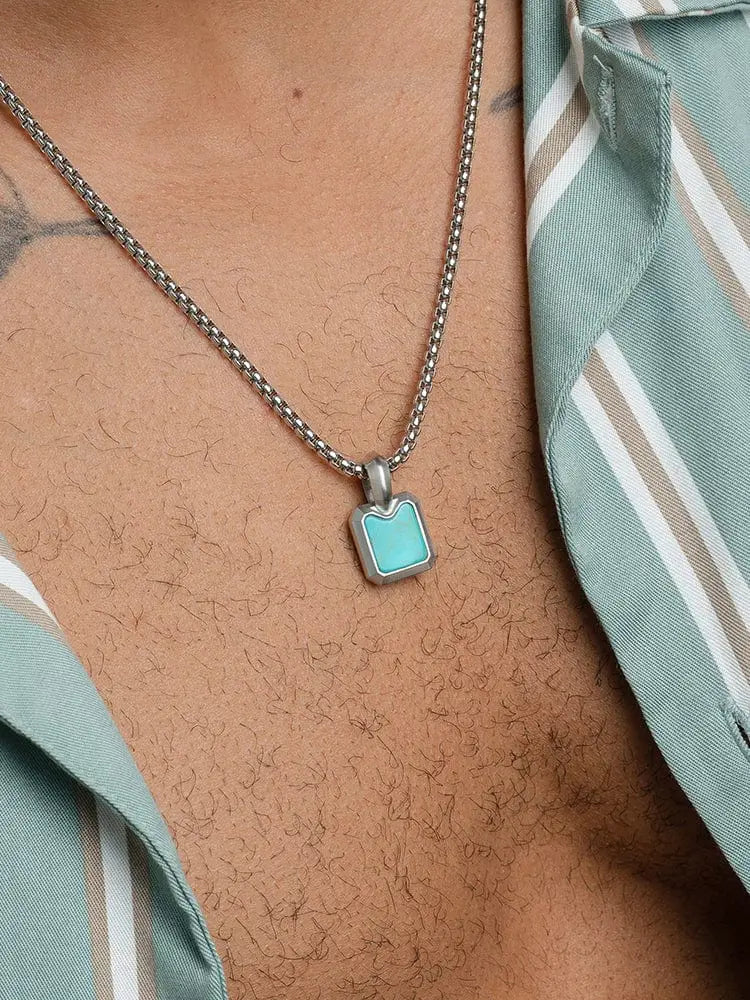 A brushed stainless steel silver chain necklace with a rectangular turquoise inlay pendant and subtle cutout design