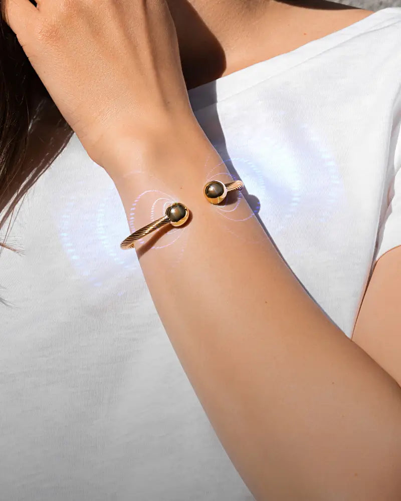 Gold twisted cable magnetic cuff bracelet in gold tone with two dark green spherical gemstones at the ends