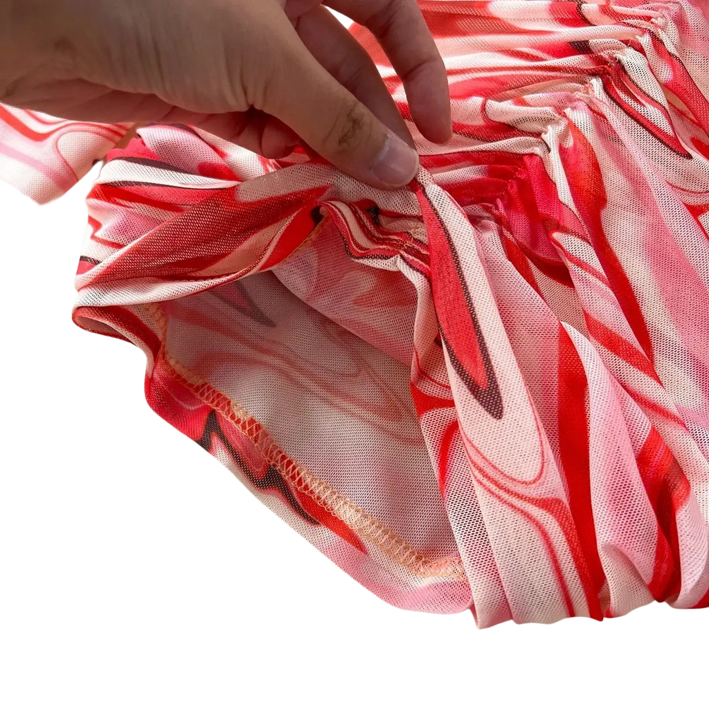 A hand gently holds the red and white mesh fabric of a two piece marble print skirt set with elastic closure