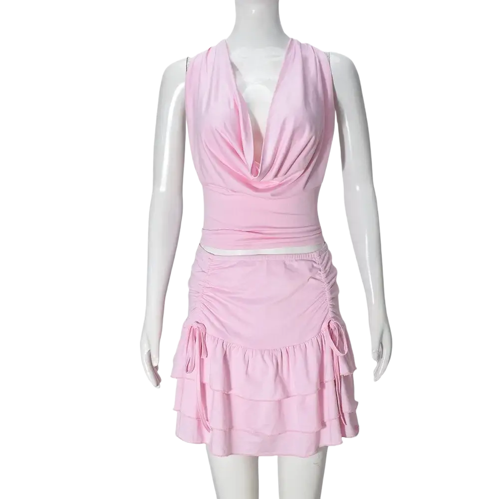 A soft pink two piece mini skirt set with pullover closure featuring a draped cowl neckline and tiered ruffle skirt