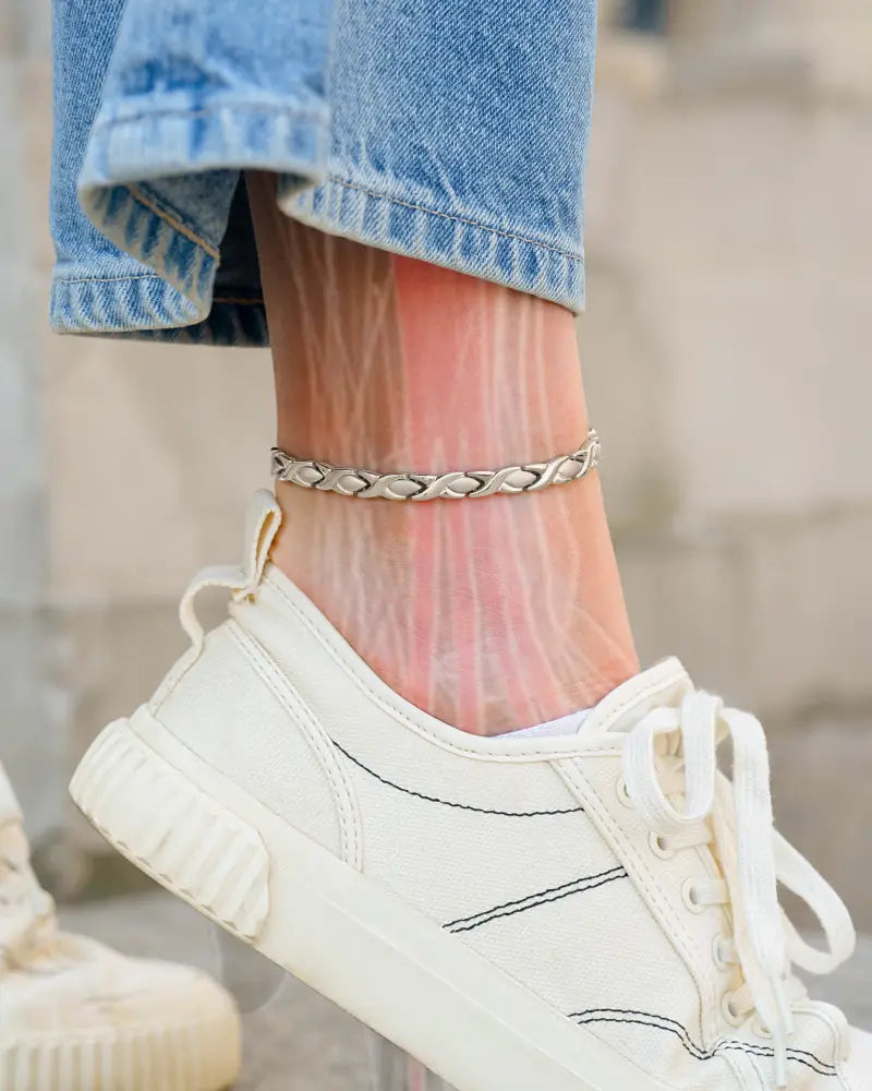 A sleek silver titanium magnetic therapy braided anklet adorns the ankle for women