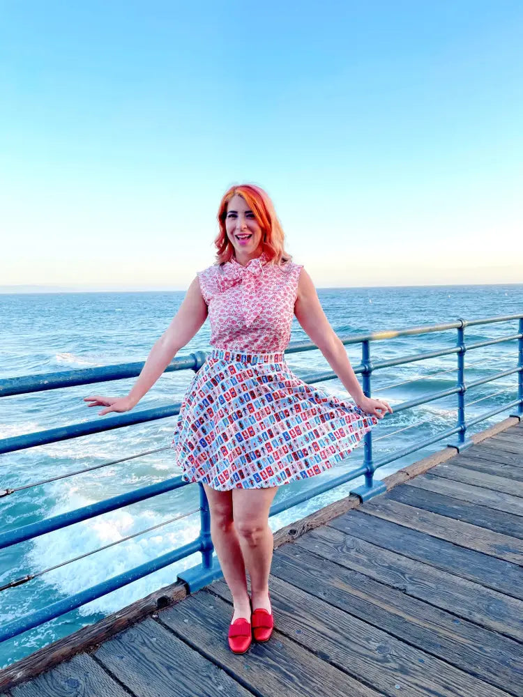 A woman wearing a vintage beach umbrella print bow neckline blouse with a pink and white patterned sleeveless dress