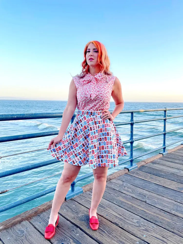 A woman wears a sleeveless pink dress with floral pattern top and flared skirt featuring colorful retro phone designs