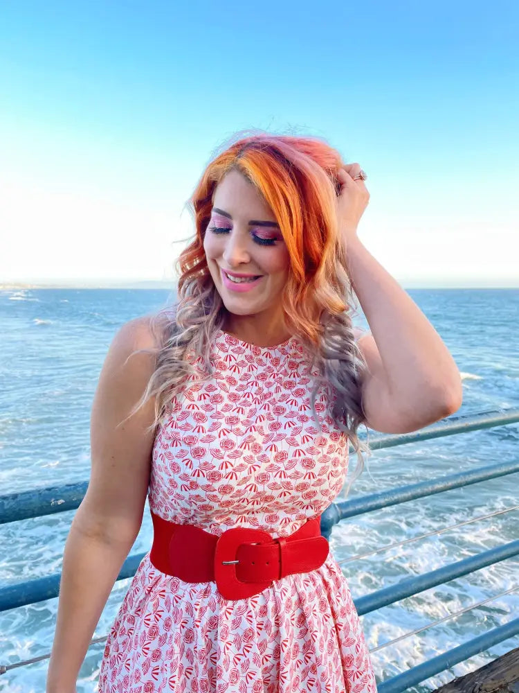 A woman wearing a sleeveless red and white patterned vintage umbrella print pink floral midi dress with a bold red belt