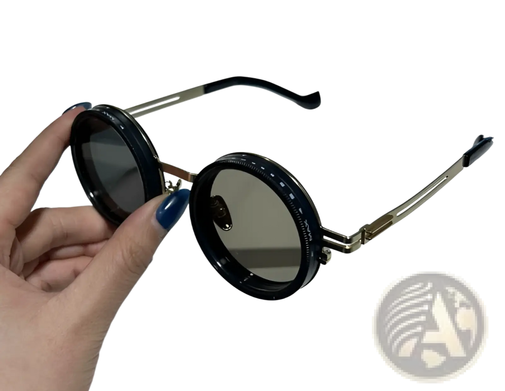 Black unisex round uv resistant sunglasses with gold-tone metal frames and dark gray lenses held by a hand