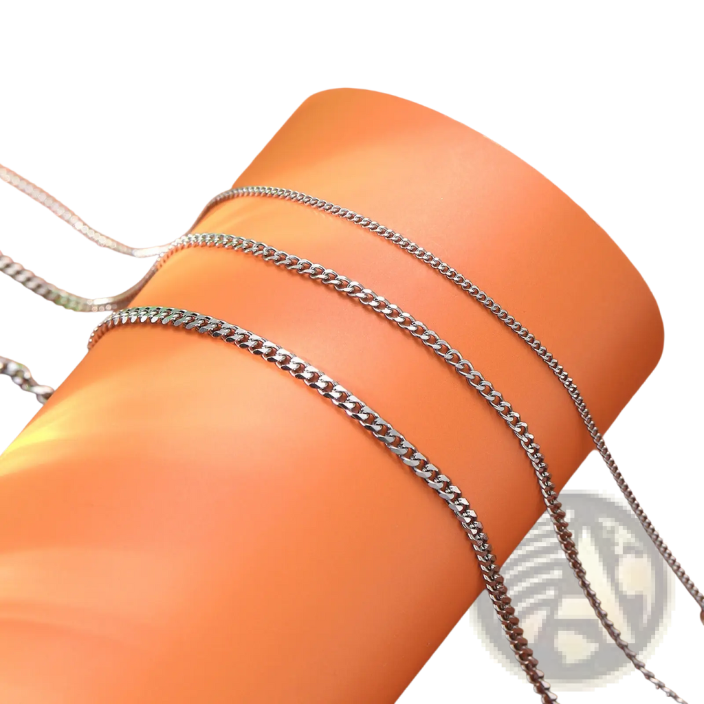 Unisex silver layered Cuban and Figaro link bracelet set with silver-toned curb chain necklaces on orange surface