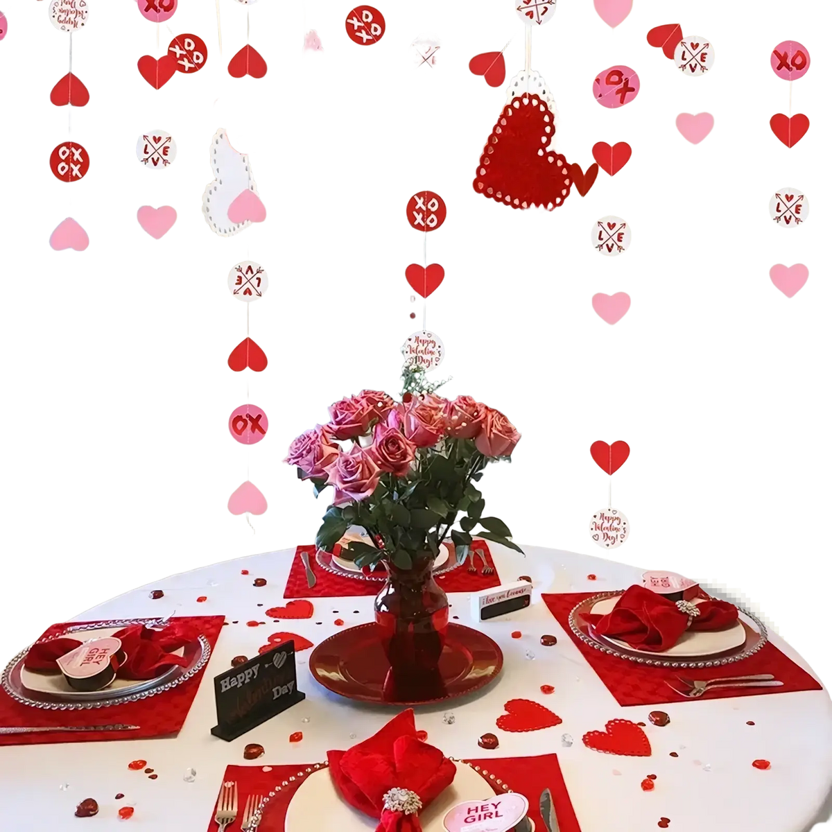 A vibrant red glass vase holding pink roses surrounded by valentine heart garland party banner decorations