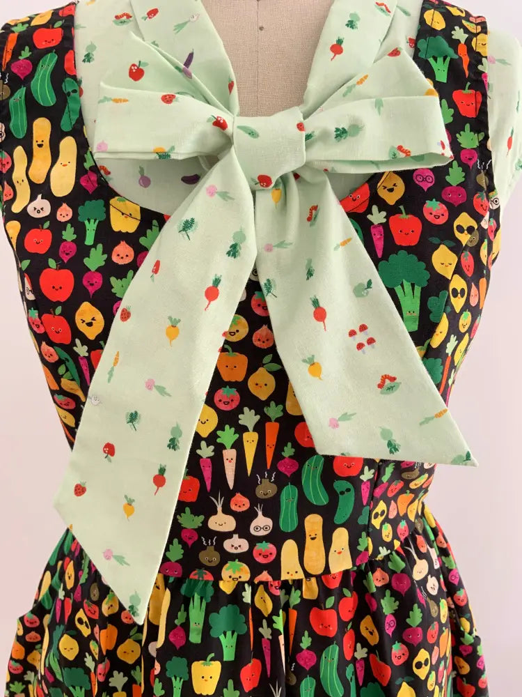 A vintage green veggie print bow blouse with a mint green bow tie and colorful smiling vegetable print on black fabric