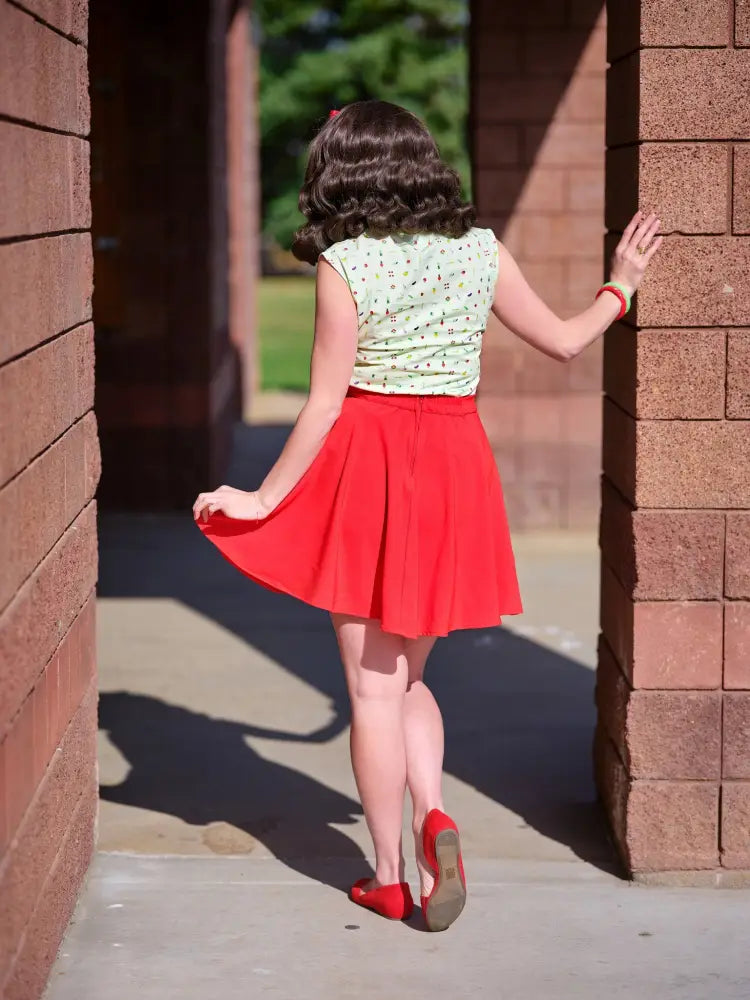 A woman wearing a vintage green veggie print bow blouse paired with a red pleated skirt and matching red shoes