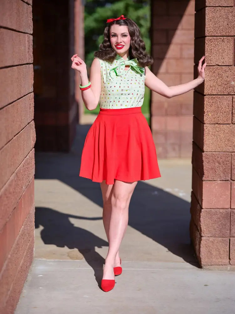 A woman wearing a vintage green polka-dot sleeveless blouse with a bow paired with a red pleated skirt