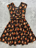 A vintage floral Greta cotton v neck knee length dress in black with orange and white blossoms, short sleeves, and cinched waist