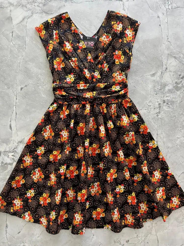 A vintage floral Greta cotton v neck knee length dress in black with orange and white blossoms, short sleeves, and cinched waist