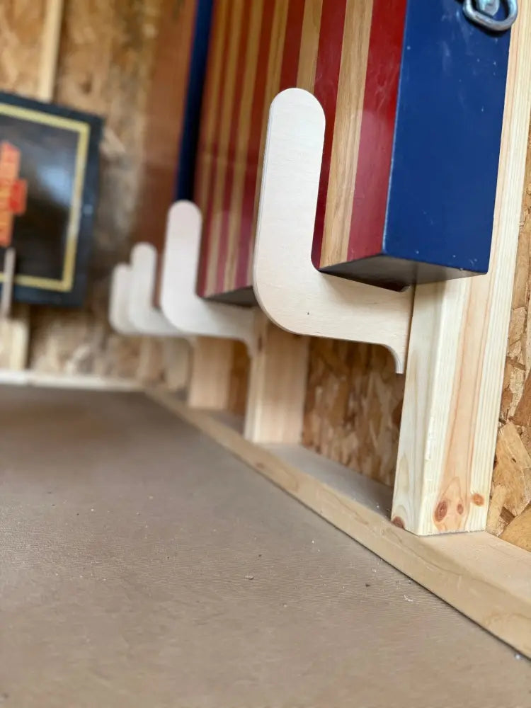 Birch plywood wall mounted cornhole board storage brackets with wooden cactus shaped hooks on a wall