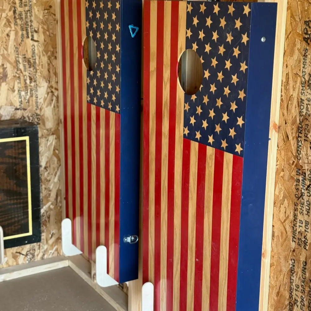 Birch plywood wall mounted cornhole board storage brackets holding american flag themed wooden cornhole boards with stars and stripes