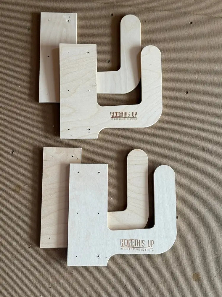 Light-colored birch plywood wall mounted cornhole board storage brackets with minimalist l-shaped design and engraved branding