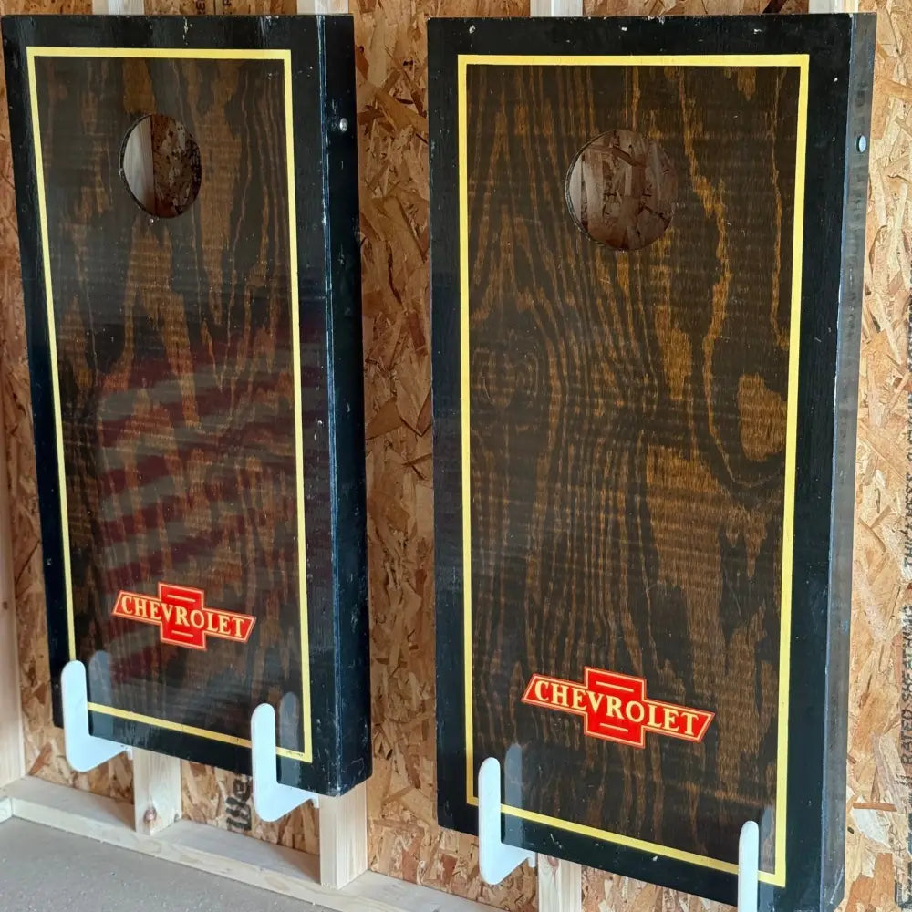 Dark wood-paneled cornhole boards with yellow border and red chevrolet logo stored on birch plywood wall mounted brackets