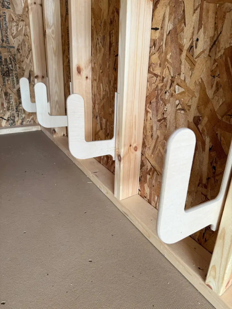 White plastic u-shaped hooks mounted on wooden framing as wall mounted storage brackets for birch plywood cornhole boards