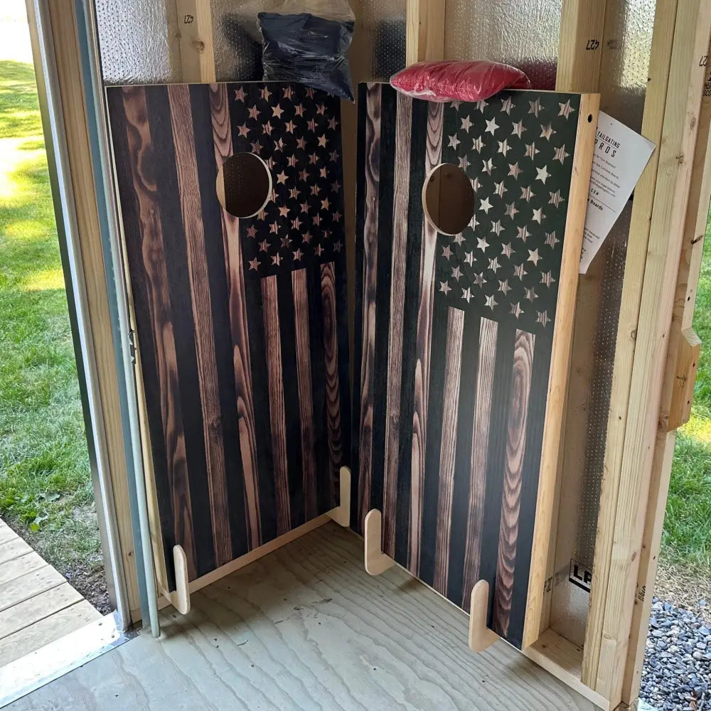 Two wooden cornhole boards with distressed american flag design stored on birch plywood wall mounted cornhole board brackets