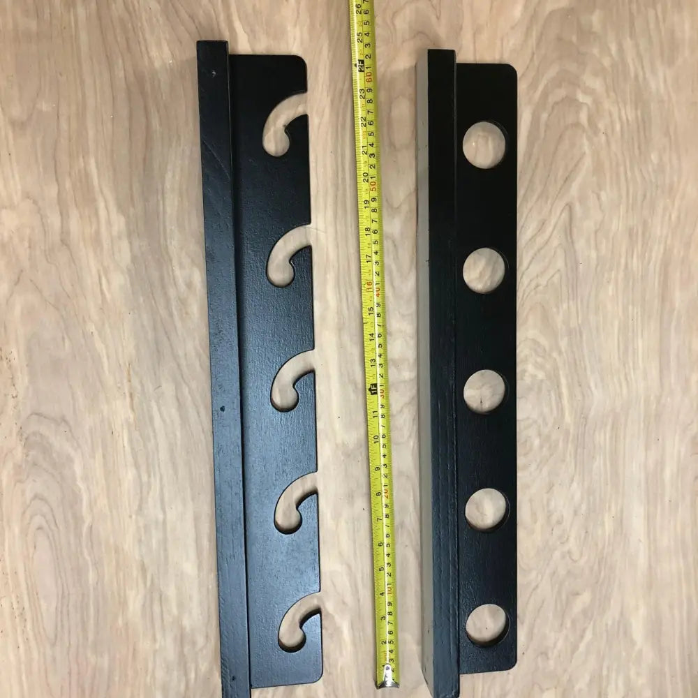 Black metal wall-mounted cue stick holders with decorative scrollwork and circular cutouts for fishing rod storage