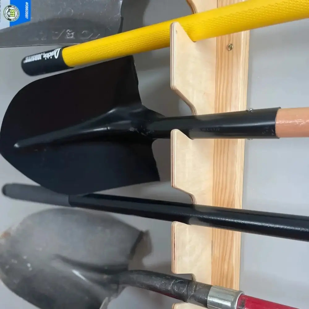 Black metal shovel with yellow handle mounted on lancaster wooden wall mounted garden tool and shovel rack