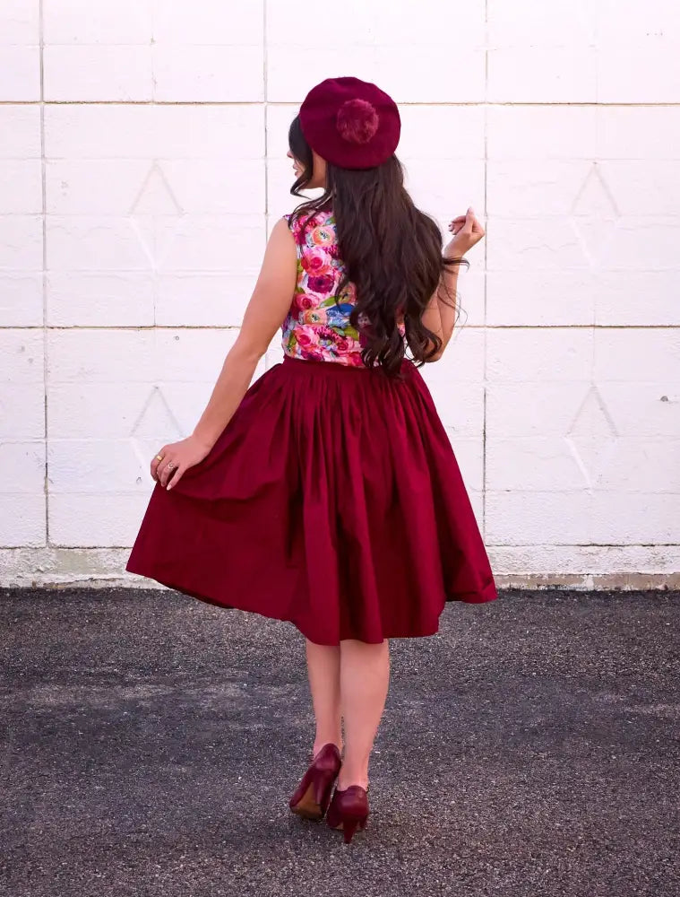 A woman wears a vintage watercolor floral halter top with oversized bow paired with a vibrant red satin skirt and maroon beret
