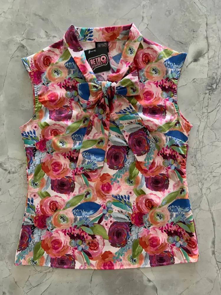 A vibrant sleeveless floral blouse with an oversized bow at the neckline featuring pink red and blue blossoms on light fabric