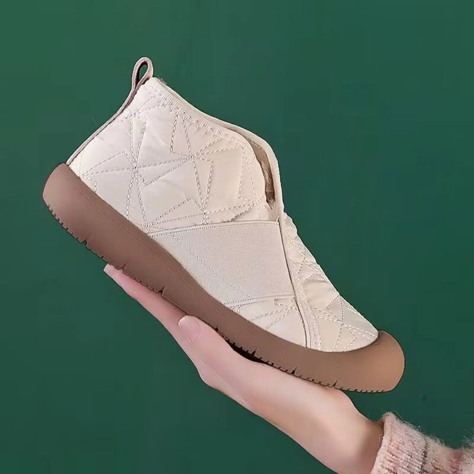 Cream-colored waterproof plush winter snow ankle boot with quilted design, brown rubber sole, and elastic side panel