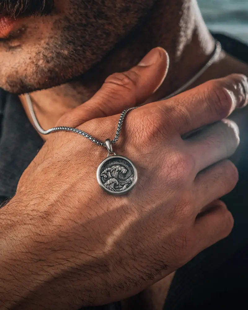Silver coin-style pendant engraved with intricate wave design on a silver box chain necklace