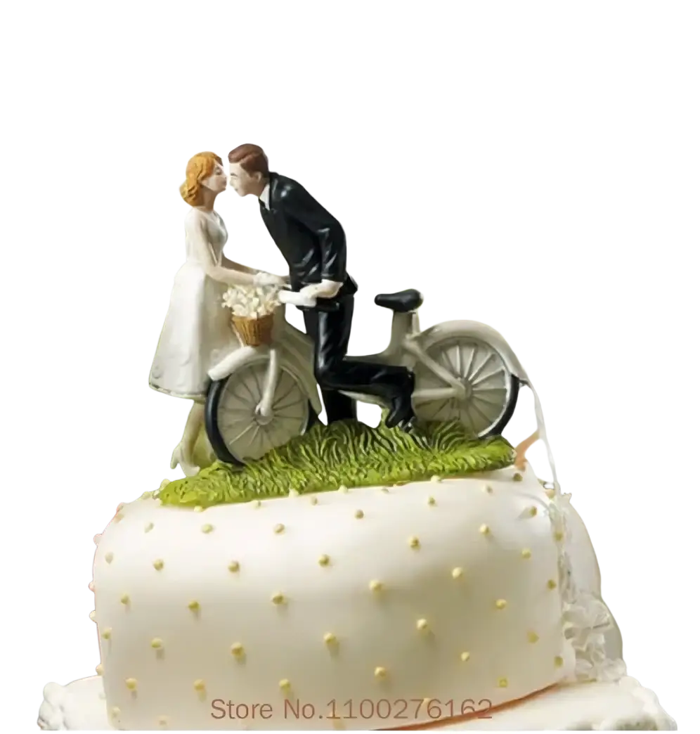 Wedding cake topper bride and groom resin figurine in white featuring couple kissing on vintage bicycle with green grass base