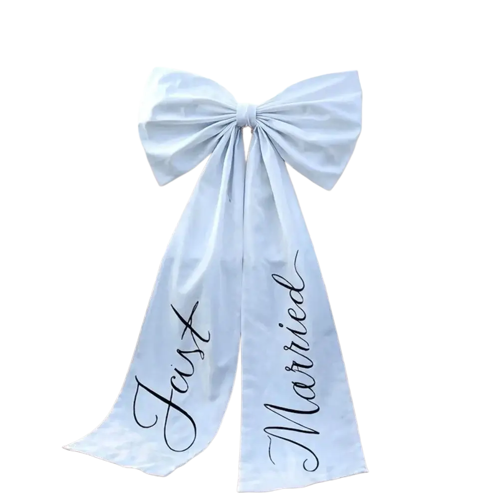 A light blue satin wedding car bow with just married scripted in black cursive tied on the back of a vintage white car