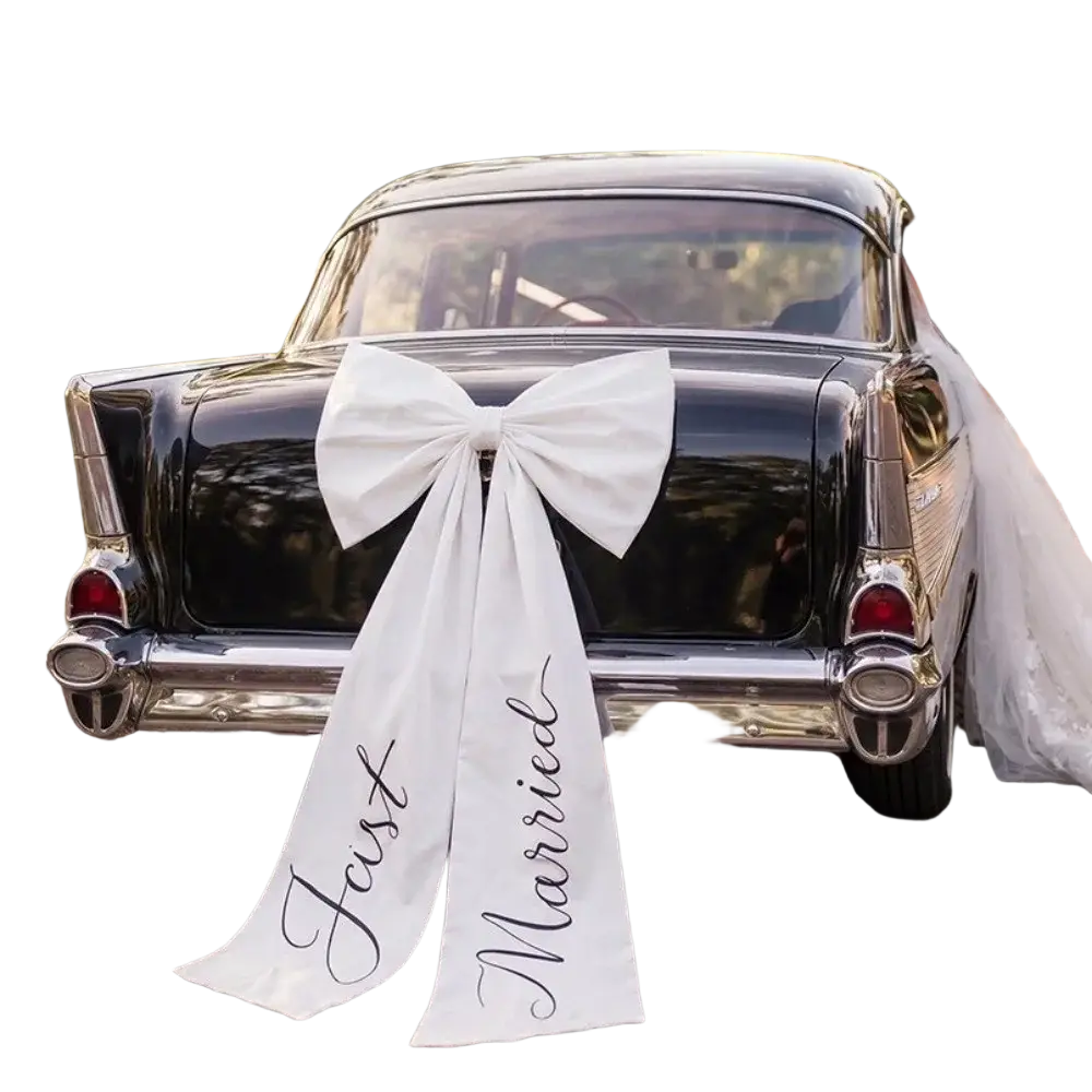 Large white satin wedding car bow with just married scripted in black cursive on the rear of a classic black car